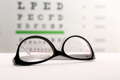 Photo of Glasses with corrective lenses on table against eye chart