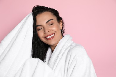 Photo of Beautiful young woman in bathrobe drying hair with towel on pink background