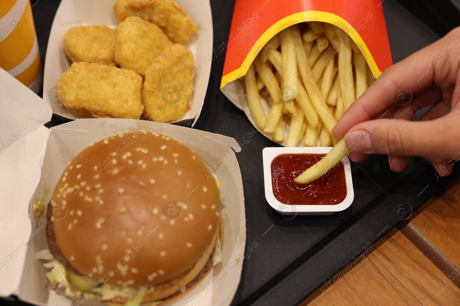 Photo of Lviv, Ukraine - October 9, 2023: Woman dipping McDonald's french fry into sauce at wooden table, closeup