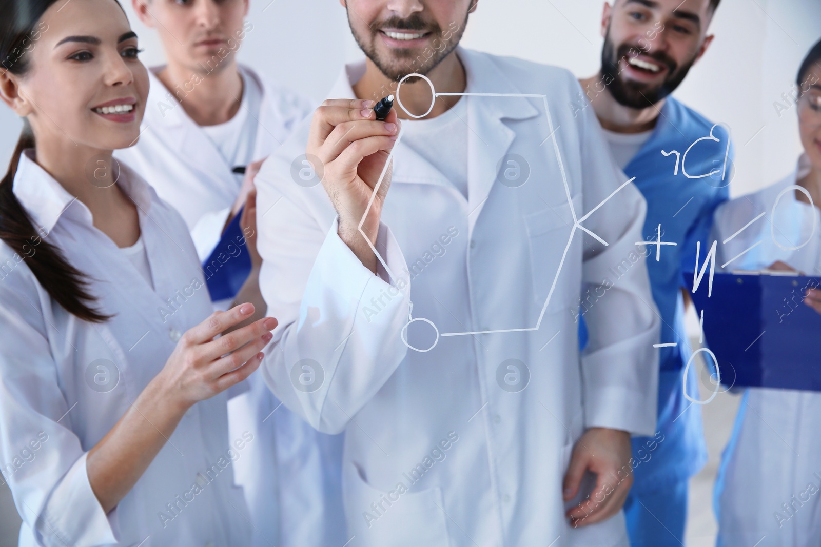 Photo of Medical students writing chemical formula on glass whiteboard in laboratory