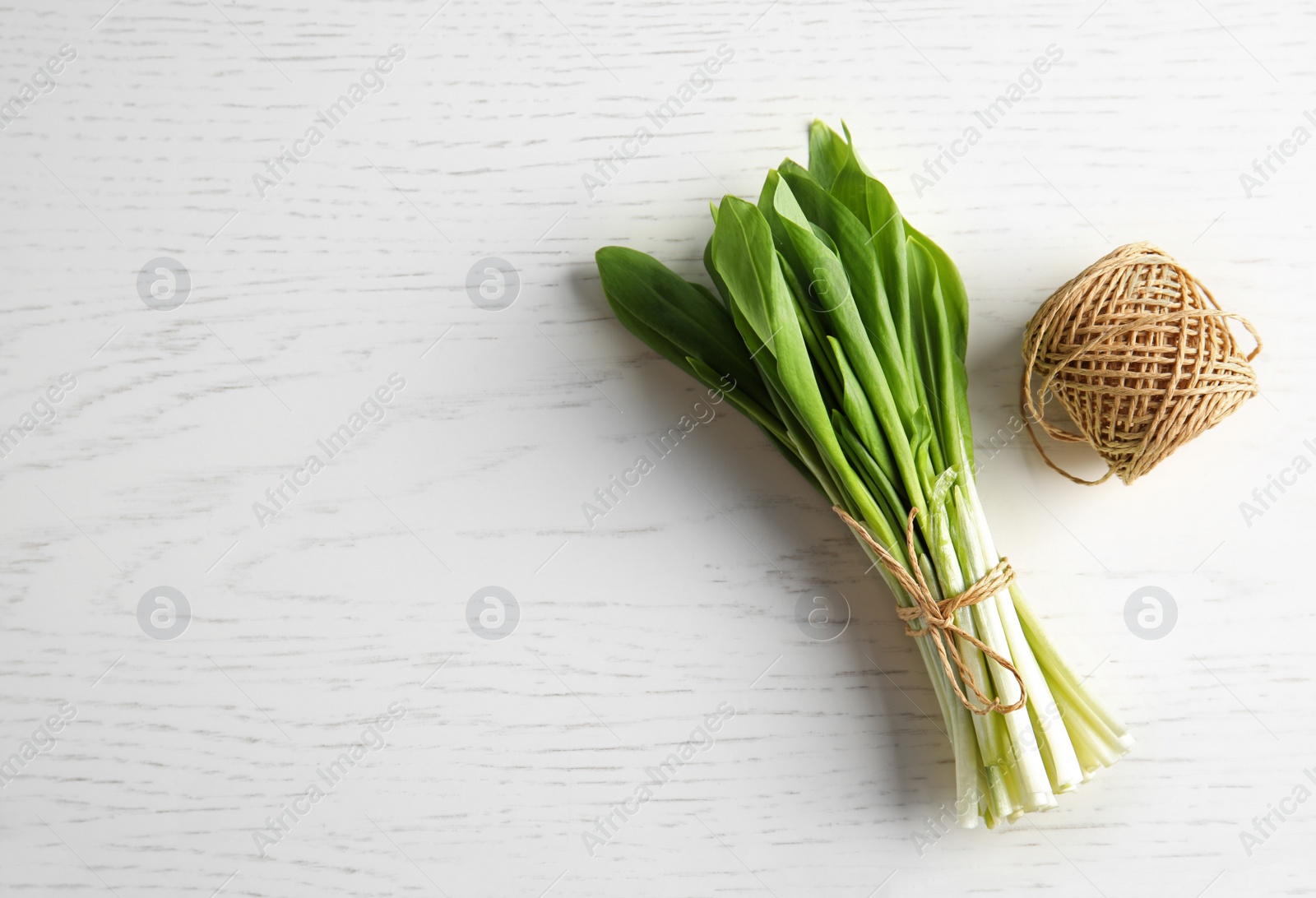 Photo of Bunch of wild garlic or ramson and thread on wooden table, top view with space for text