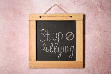 Photo of Blackboard with phrase Stop Bullying and prohibition sign on pink wall