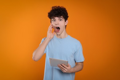 Photo of Portrait of shocked teenage boy with tablet on orange background