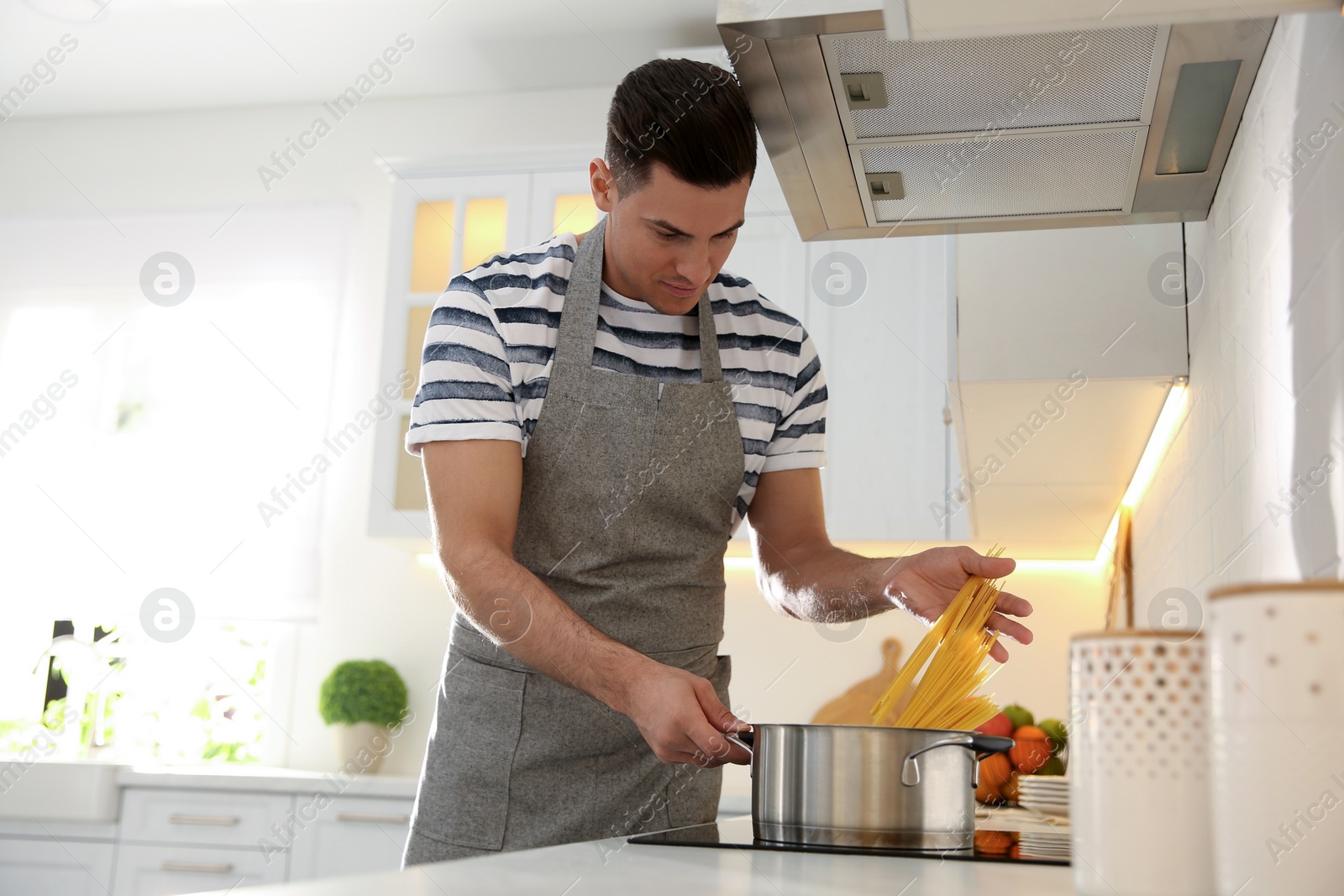 Photo of Handsome man cooking pasta on stove in kitchen