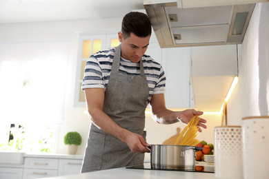 Handsome man cooking pasta on stove in kitchen