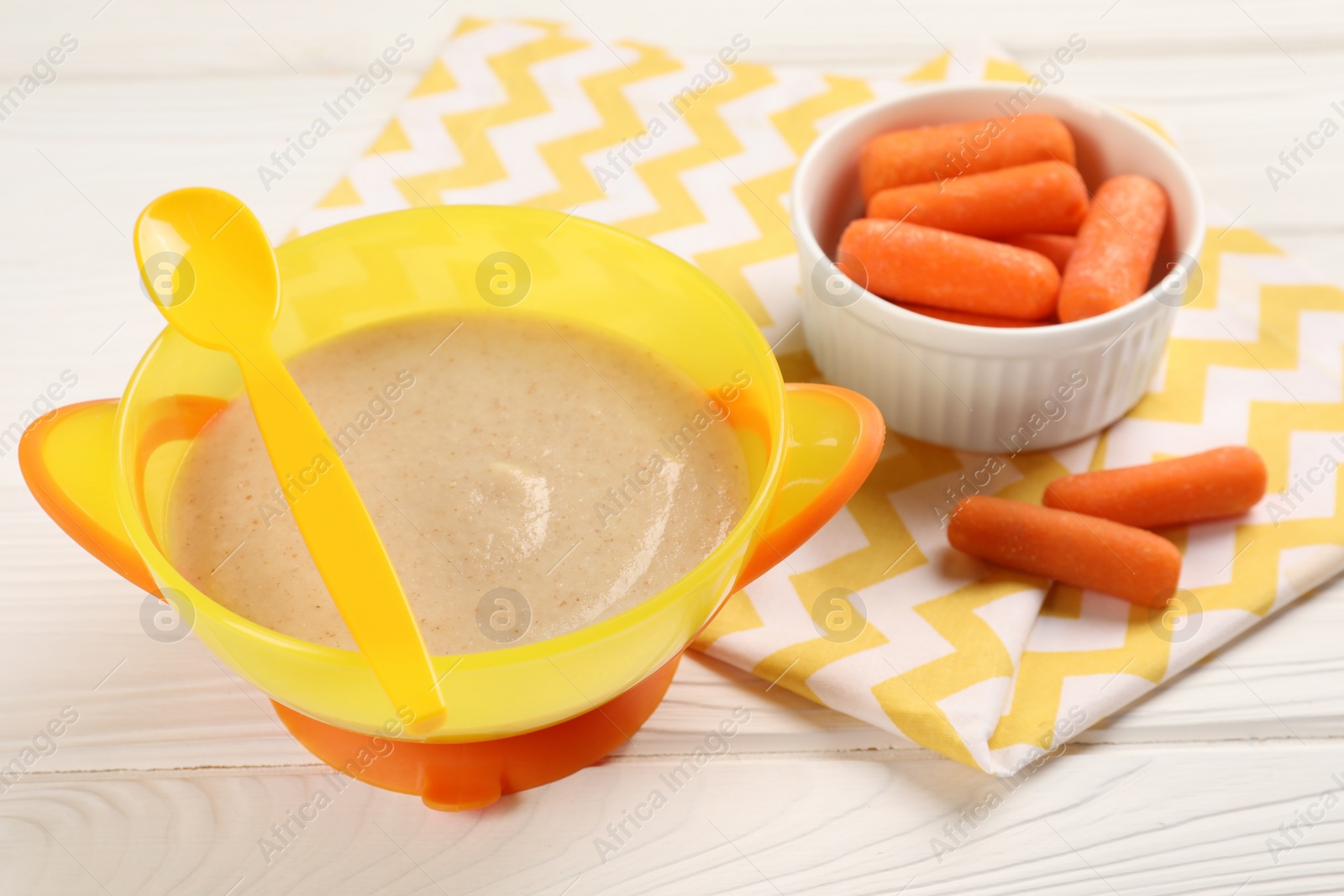 Photo of Baby food. Puree in bowl and small carrots on white wooden table