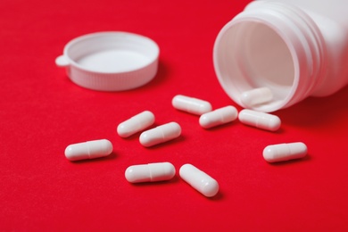 Photo of Scattered pills and container on color background. Heart disease concept