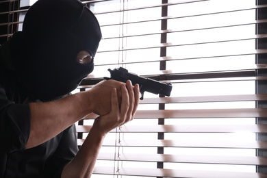 Photo of Man in mask aiming through window blinds indoors