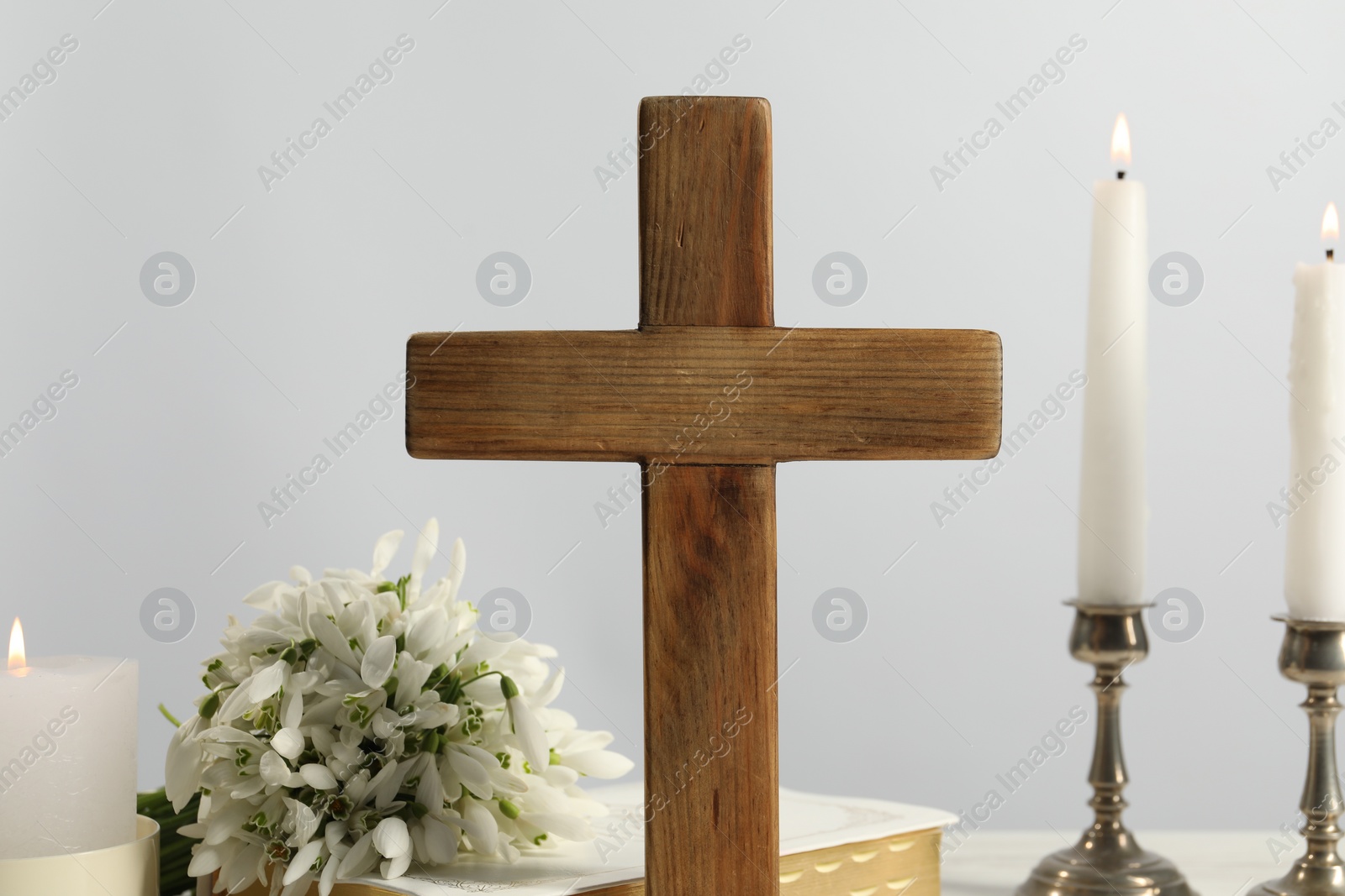 Photo of Burning church candles, wooden cross, Bible and flowers on table, closeup