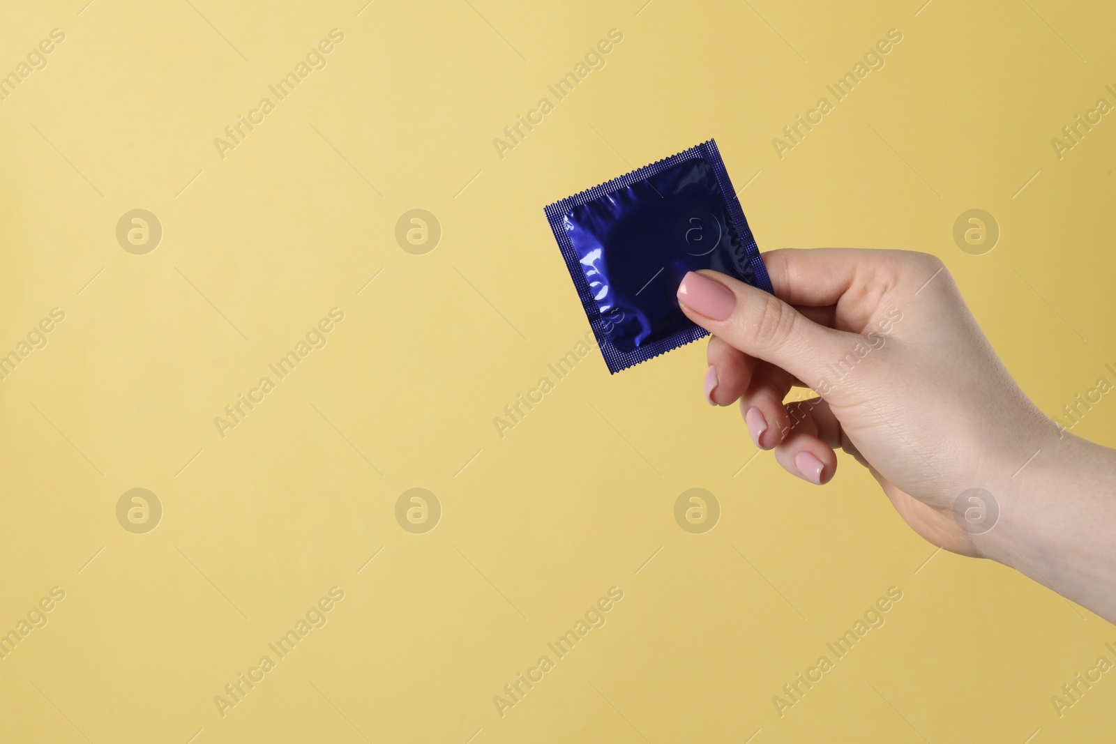 Photo of Woman holding condom on pale yellow background, closeup. Space for text