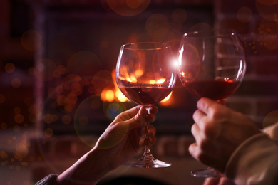Image of Lovely couple with glasses of wine near fireplace indoors, closeup. Winter vacation