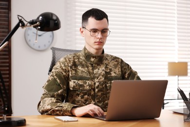 Photo of Military service. Young soldier working with laptop at wooden table in office