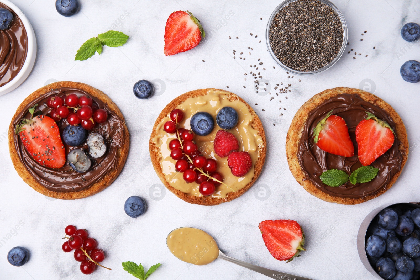 Photo of Tasty organic rusks with different toppings and ingredients on white marble table, flat lay