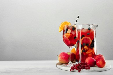 Photo of Glass and jug of Red Sangria on white wooden table against light grey background. Space for text