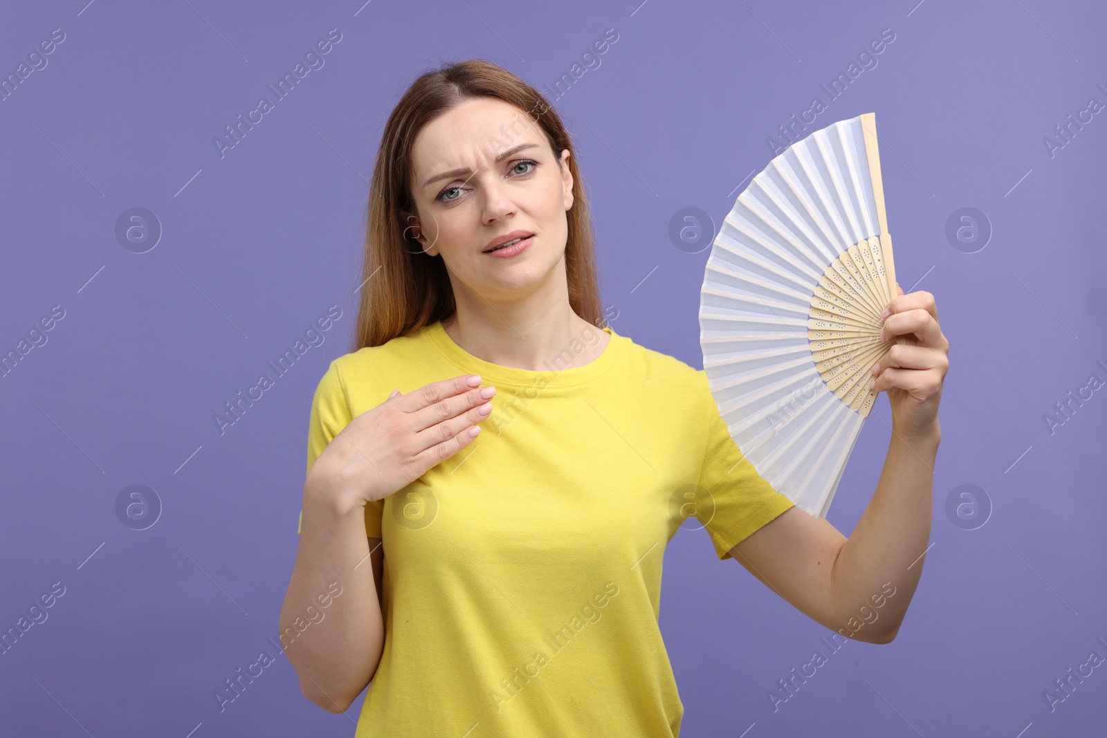 Photo of Beautiful woman waving hand fan to cool herself on violet background