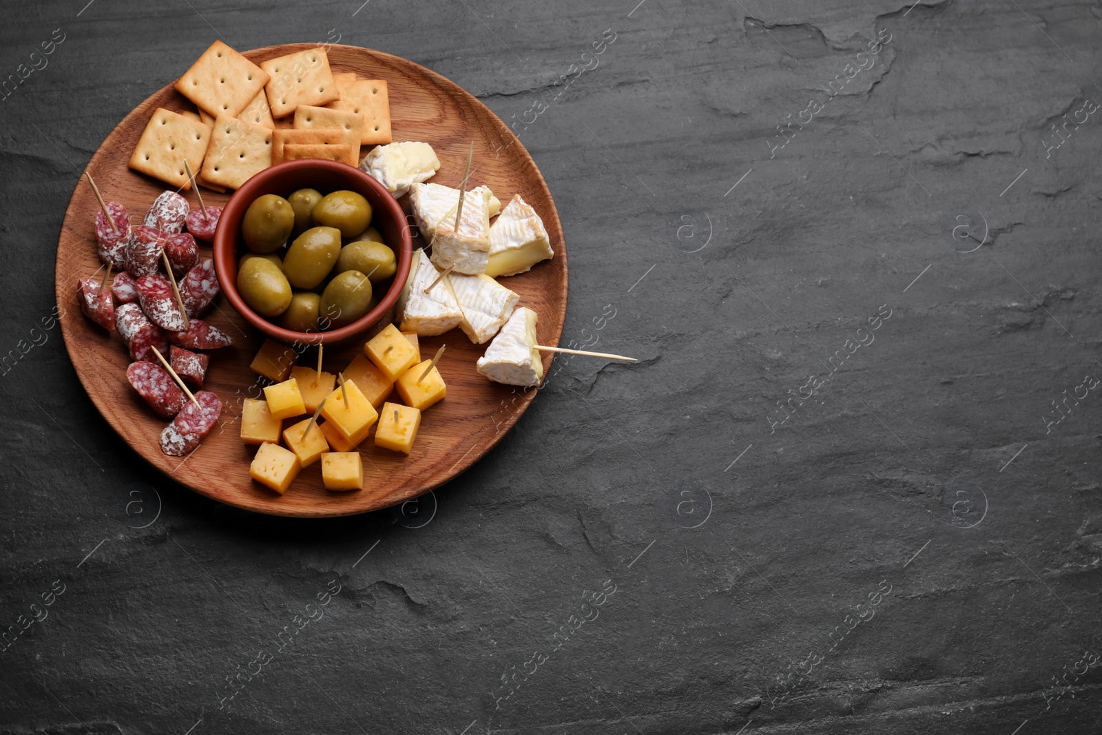 Photo of Toothpick appetizers. Pieces of cheese, sausage and olives on black table, top view with space for text