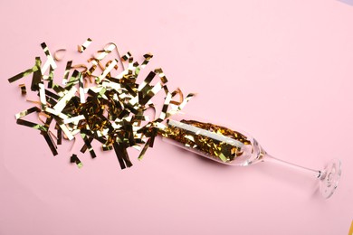 Glass and shiny confetti on pink background, flat lay