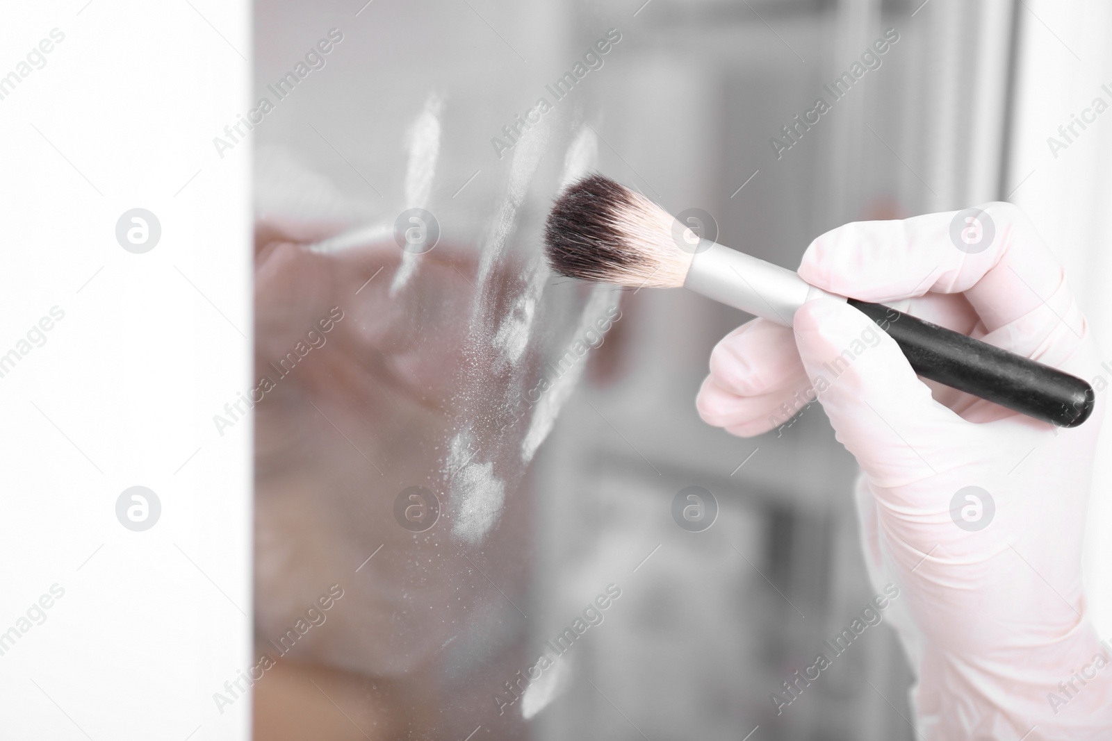 Photo of Detective using brush and powder to reveal fingerprints on glass surface indoors, closeup