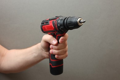 Photo of Handyman holding electric screwdriver on grey background, closeup