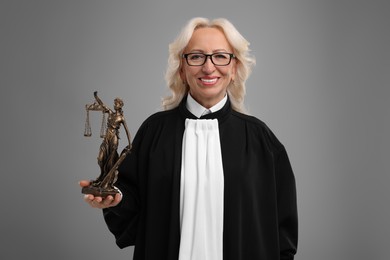 Photo of Smiling senior judge with figure of Lady Justice on grey background