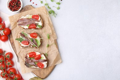 Delicious bruschettas with anchovies, tomatoes, microgreens and cream cheese on white table, flat lay. Space for text