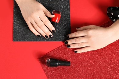 Photo of Woman with black manicure and nail polish bottles on color background, top view