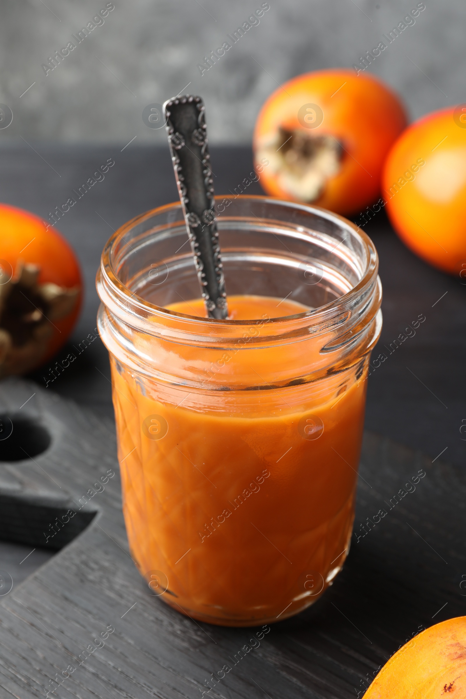 Photo of Delicious persimmon jam in glass jar served on dark gray wooden table