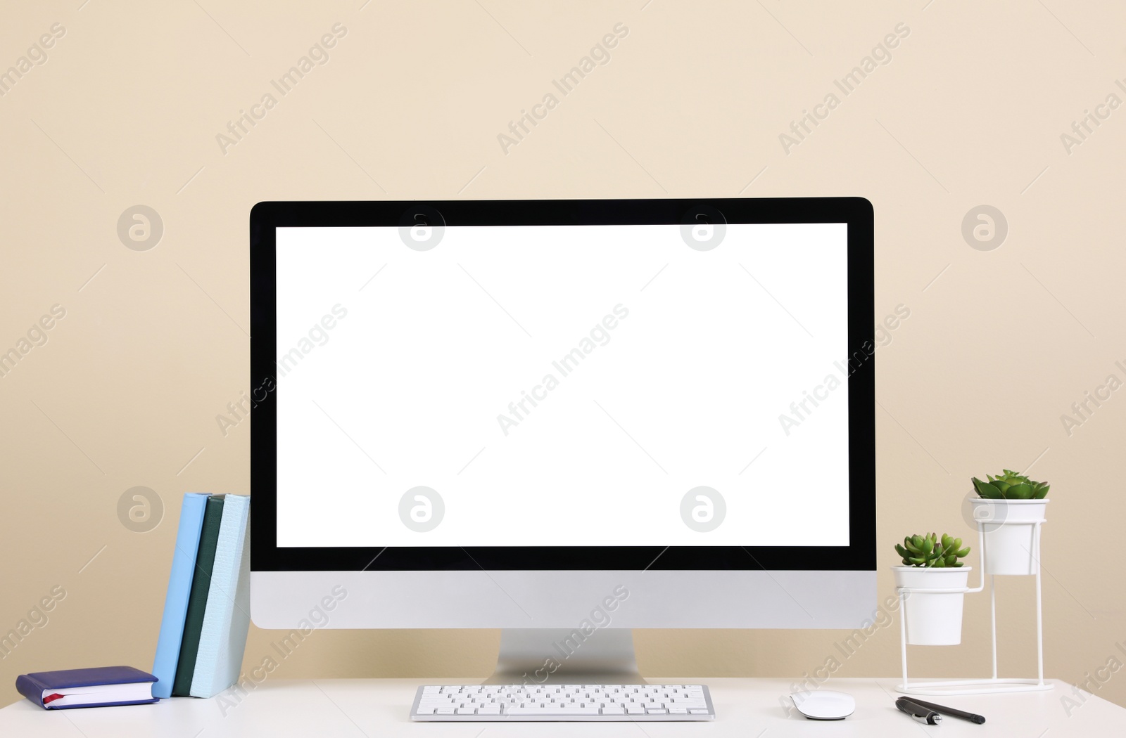 Photo of Comfortable workplace with blank computer display on desk near beige wall. Space for text