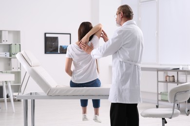 Professional orthopedist examining patient's shoulder in clinic