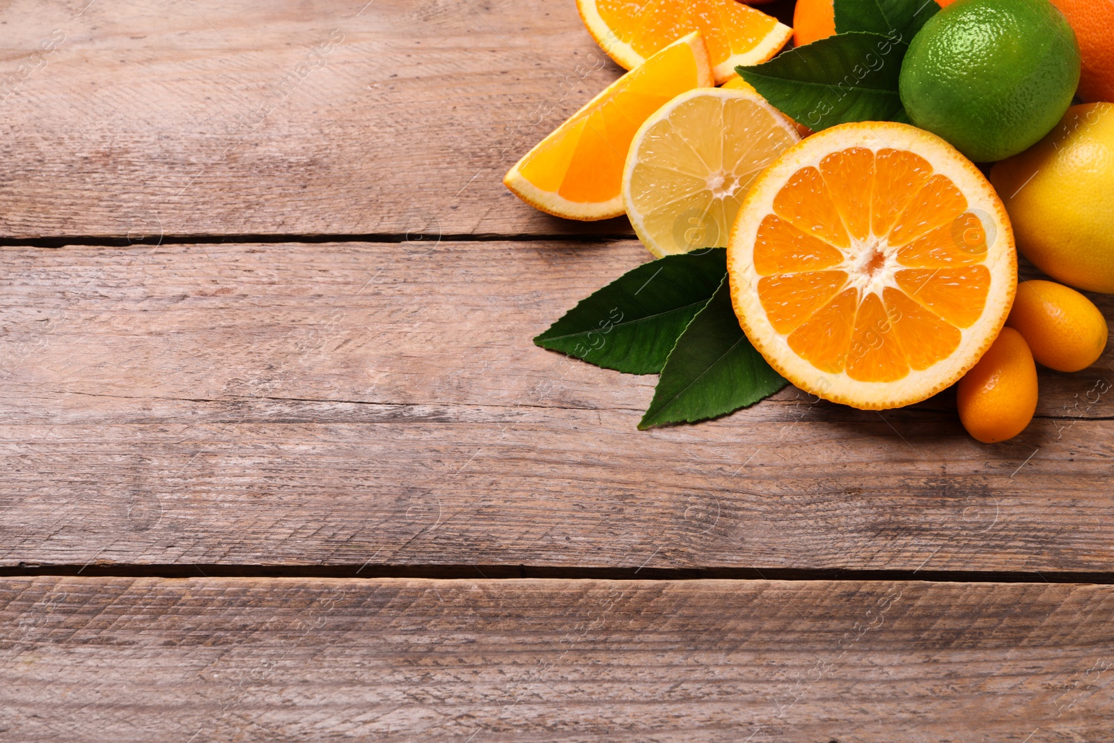 Photo of Fresh juicy citrus fruits with green leaves on wooden table, above view. Space for text