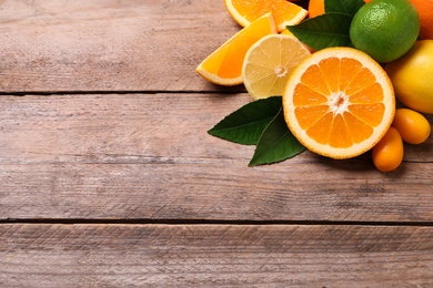 Photo of Fresh juicy citrus fruits with green leaves on wooden table, above view. Space for text