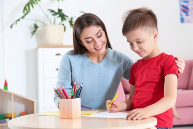 Photo of Cute little child drawing at table with his mother in playing room