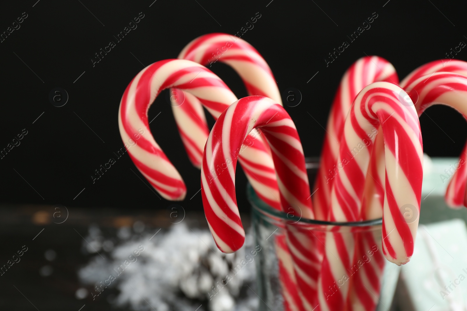 Photo of Many sweet candy canes in glass on black background, closeup. Traditional Christmas treat
