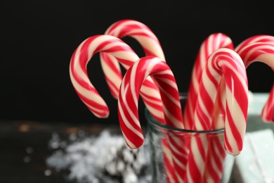 Photo of Many sweet candy canes in glass on black background, closeup. Traditional Christmas treat