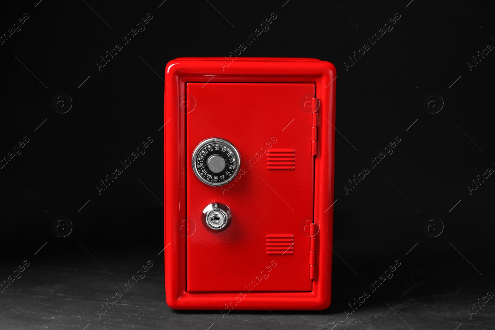 Photo of Red steel safe with mechanical combination lock against black background