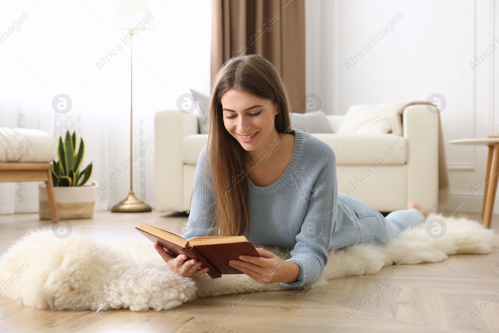 Photo of Beautiful young woman reading book at home. Floor heating concept