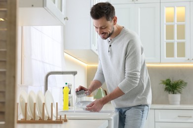 Photo of Man washing plate above sink in kitchen