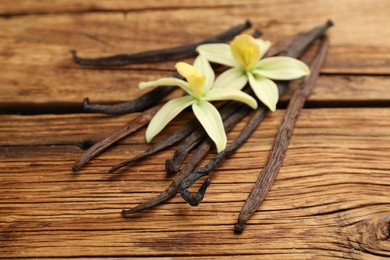 Photo of Aromatic vanilla sticks and flowers on wooden table, closeup