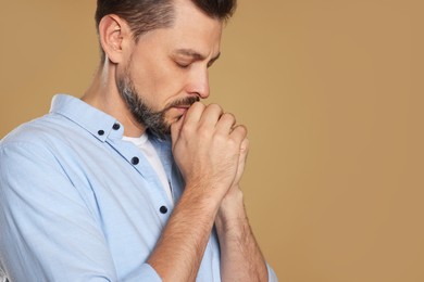 Photo of Man with clasped hands praying on beige background, closeup. Space for text