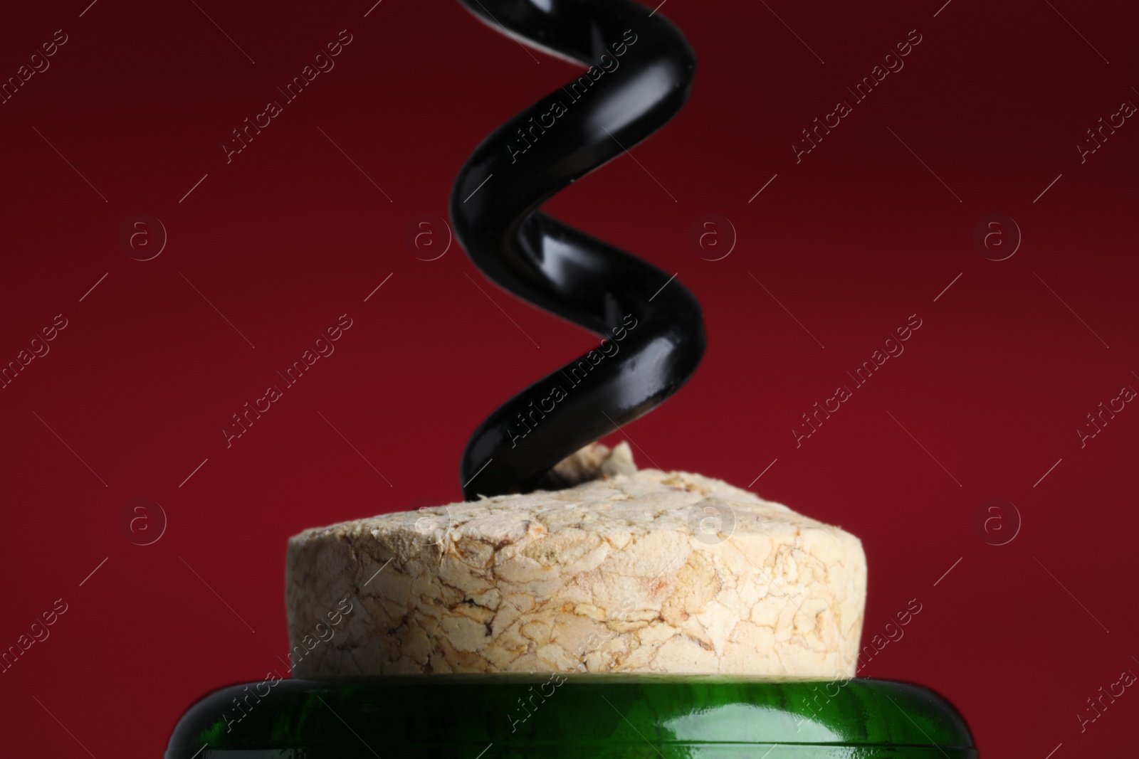 Photo of Opening bottle of wine with corkscrew on burgundy background, closeup