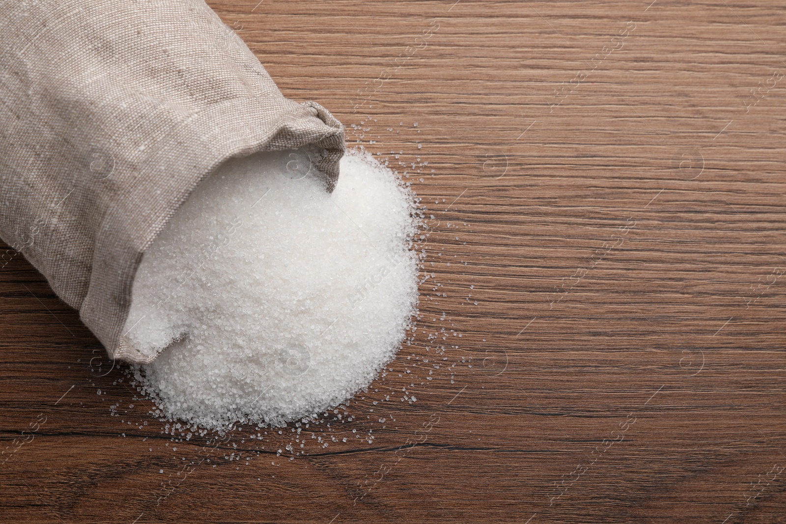 Photo of Overturned sack bag with granulated sugar on wooden table, top view. Space for text