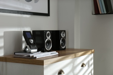 Photo of Modern powerful audio speakers and remote on chest of drawers indoors