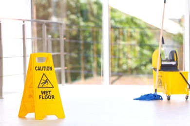 Safety sign with phrase Caution wet floor and mop bucket, indoors. Cleaning service