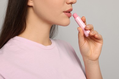 Young woman applying lip balm on grey background, closeup