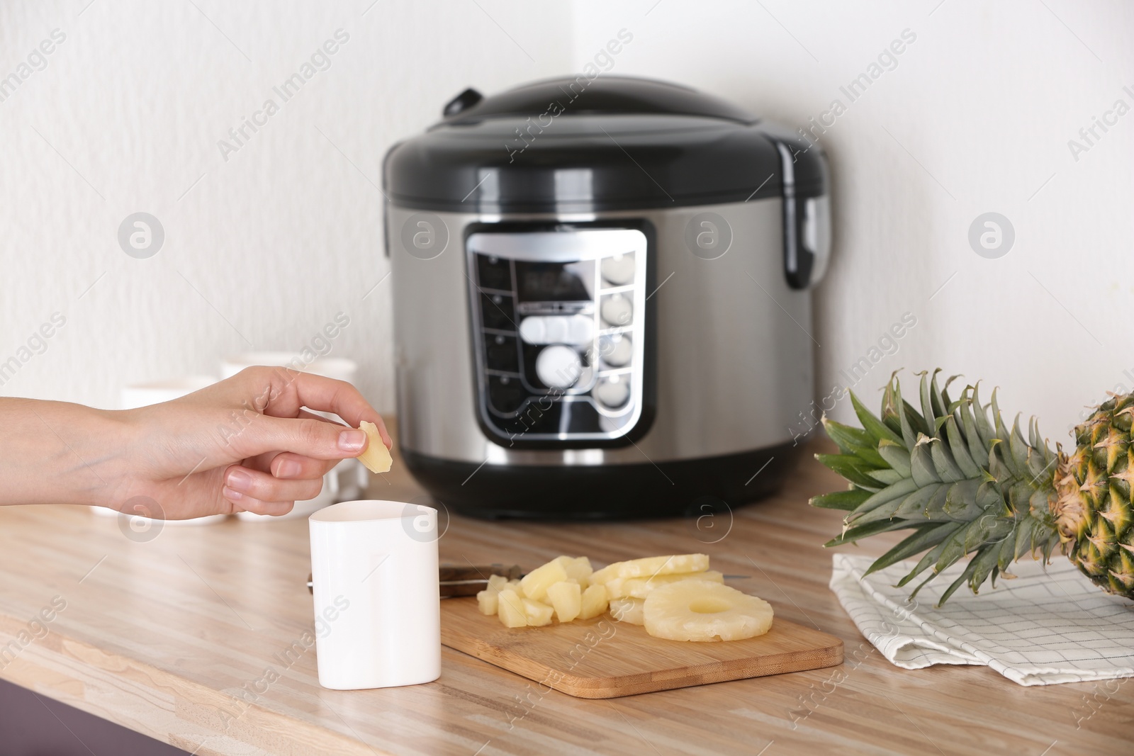 Photo of Woman putting pineapple into container with delicious fresh yogurt made in modern multi cooker on table, closeup