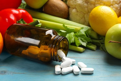 Photo of Dietary supplements. Overturned bottle with pills near food products on light blue wooden table