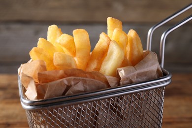 Photo of Tasty French fries in metal basket on table, closeup