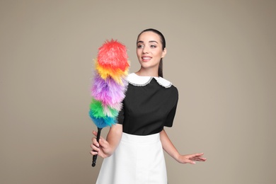 Photo of Young chambermaid with dusting brush on color background