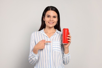 Beautiful young woman holding tin can with beverage on light grey background