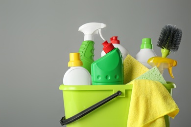 Photo of Bucket with cleaning products and tools on grey background, closeup